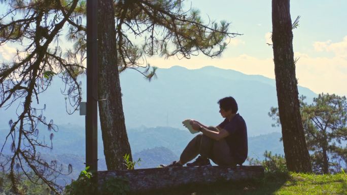 数字游牧民和旅行的概念与单独的自由职业者男人坐在木头和使用平板电脑工作从户外层山的背景