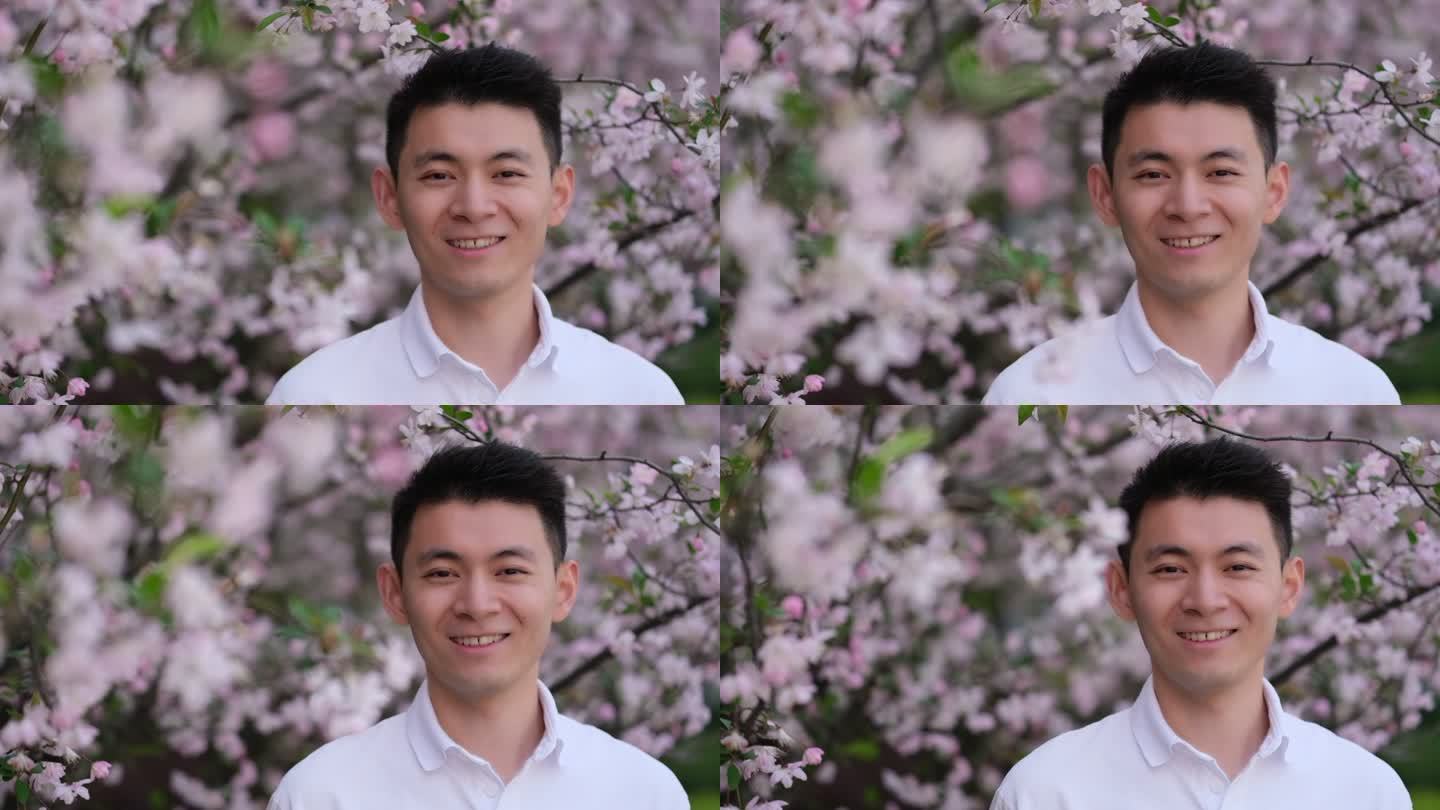 年轻中国帅哥高兴的笑，在春天户外樱花树下