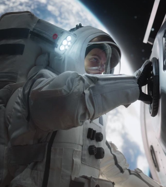 垂直屏幕:年轻的宇航员在宇宙飞船、卫星或空间站外的太空行走中穿着宇航服摆姿势。宇航员看着摄像机，微笑