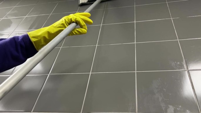 一家清洁公司用湿拖把清洗灰色瓷砖墙