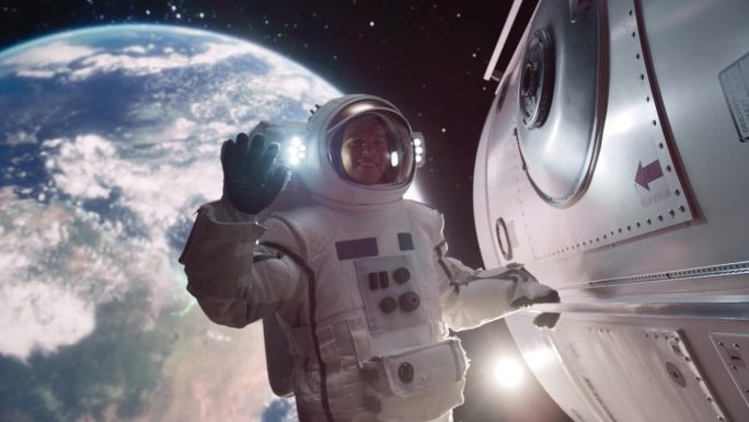 一名宇航员漂浮在宇宙飞船外的肖像，背景是地球。男:对着镜头挥手。职业太空人穿着太空服，微笑着摆姿势