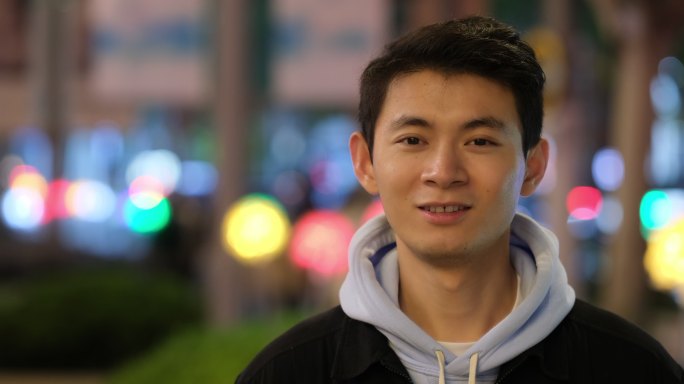 年轻中国帅哥快乐的正面笑脸，在夜晚的街头