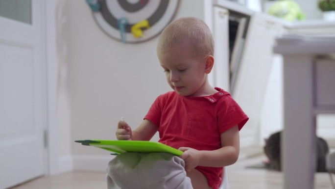 小孩子在玩小朋友用的绘图板，3岁的男孩坐在便盆上拿着电子绘图板