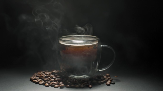 热咖啡杯概念。特写玻璃咖啡杯，杯子有漂亮的热气，豆子，黑色背景