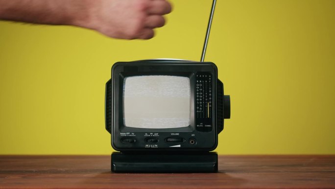打开黄色背景上有灰色干扰屏的小旧电视。桌上老式电视的特写，怀旧。灰色噪音屏幕和故障。