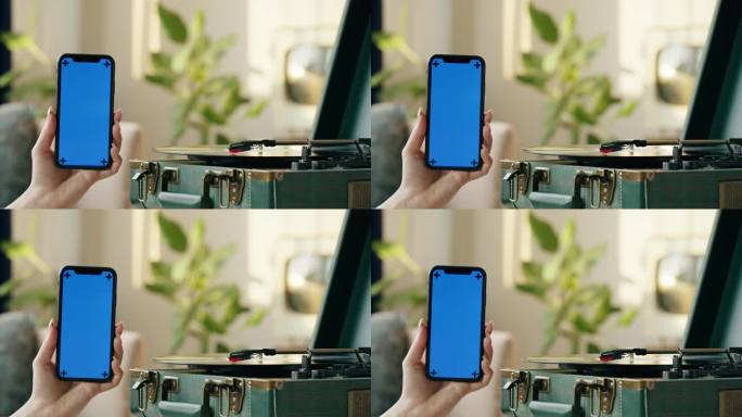 黑胶唱片特写。复古复古的黑色唱机旋转，使用智能手机与蓝色色度键屏幕。复古音乐播放器在客厅的家庭背景。