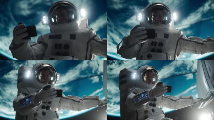 一个年轻的宇航员在零重力下漂浮在太空中的肖像。宇航员在轨道飞船外用智能手机观看视频。男子上网，连接卫
