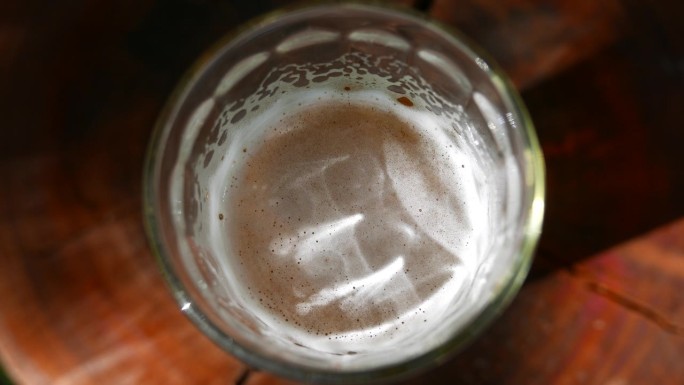 慢慢放大:桌子上的一杯啤酒，顶部角度。在随意的阳光下喝一杯啤酒。在户外喝杯啤酒。一杯啤酒，高处观。喝