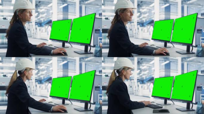在工厂办公室里，戴安全帽的白人女技术人员在带有绿屏Chromakey模拟显示器的台式电脑上工作。自主