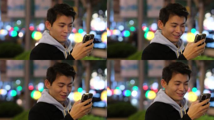 夜晚的年轻中国帅哥笑着使用智能手机