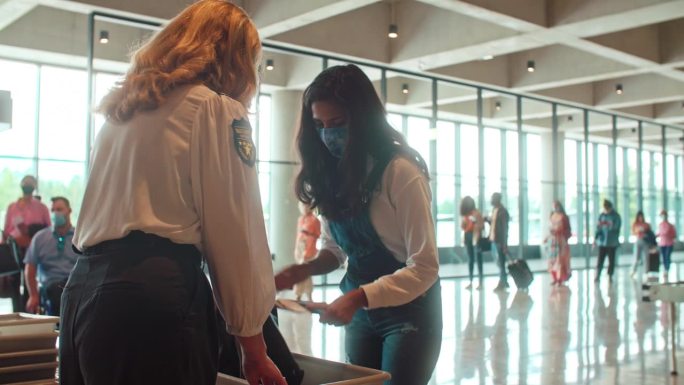 白人女保安和戴口罩的中美洲年轻旅客在行李扫描