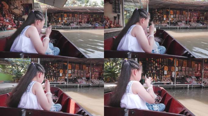 可爱的女孩在泰国水上市场的船上旅行时吃着椰子冰淇淋。