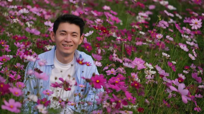 年轻中国帅哥在春天的户外花丛开心的笑