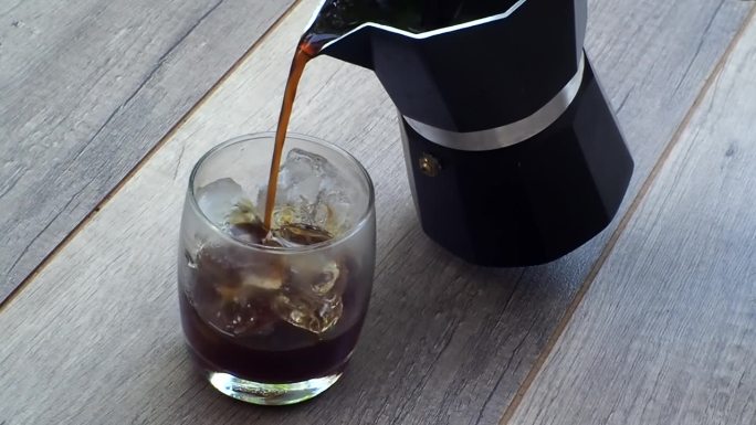 将新鲜的咖啡从摩卡壶咖啡机倒入加冰的咖啡杯。