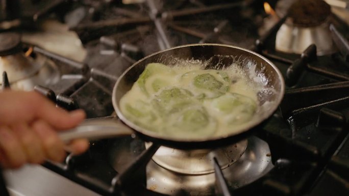 厨师把一锅绿色的意大利饺子放在火上。