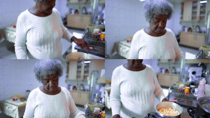 一位年长的南美黑人妇女站在厨房的炉子上煮意大利面。白发苍苍的80年代非洲裔正在准备午餐