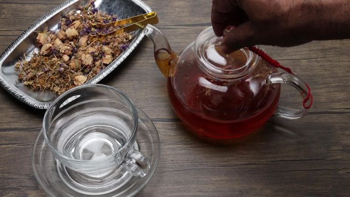 制作和倒花草茶饮透明玻璃茶壶到茶杯扭拿放在质朴的木桌