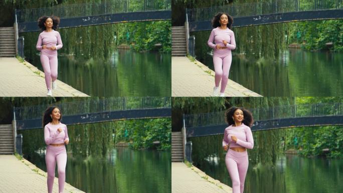 身穿粉色健身服的年轻女子沿着运河跑步穿过市区——慢镜头