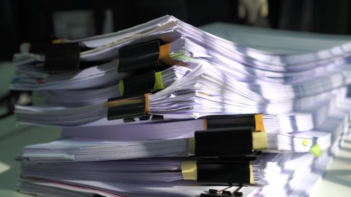 未完成的堆叠税务文件为正在处理报告文件的会计存储文件，在办公桌上有过多的计划，等待管理层批准信息，库