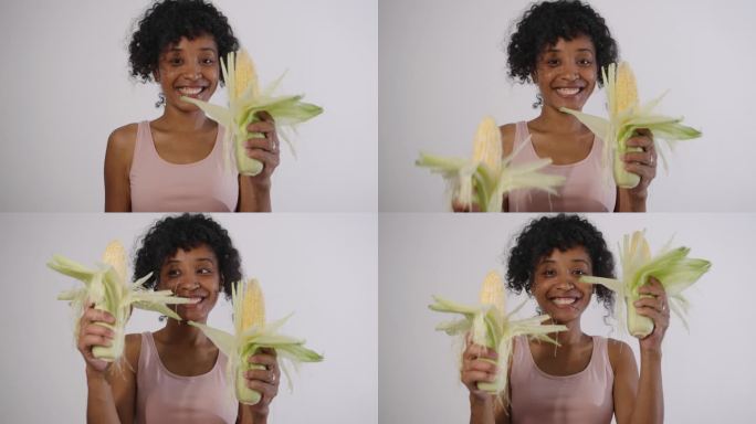 在浅色背景下，一个混血妇女的肖像，她手里拿着玉米棒，有益健康的有机产品，健康的蔬菜。