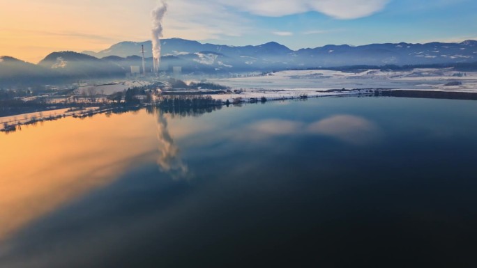 空中无人机倾斜拍摄平静的Velenje湖附近Šoštanj发电厂在冬天日出时对山冒烟