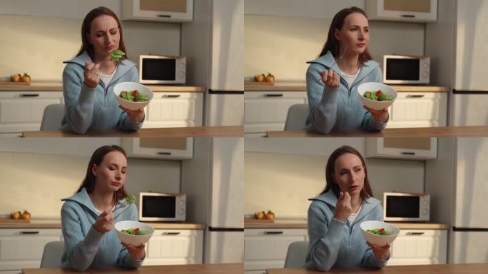 食欲不振。一个不开心的女人坐在厨房里，手里拿着叉子，端着一份蔬菜沙拉。失去味觉和嗅觉