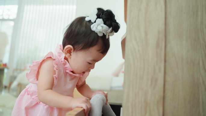 一个穿着粉色裙子的亚洲小女孩站在一个敞开的抽屉柜前，在里面找，试图从里面挑出她的玩具。儿童学习与发展