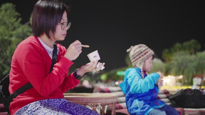 亚洲母亲和儿子晚上坐在公园里享受冰淇淋甜筒。