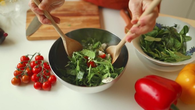 厨师高加索妇女烹饪健康食品沙拉，混合西红柿，芝麻菜，菠菜和奶酪在碗特写。健康饮食习惯，节食，素餐。
