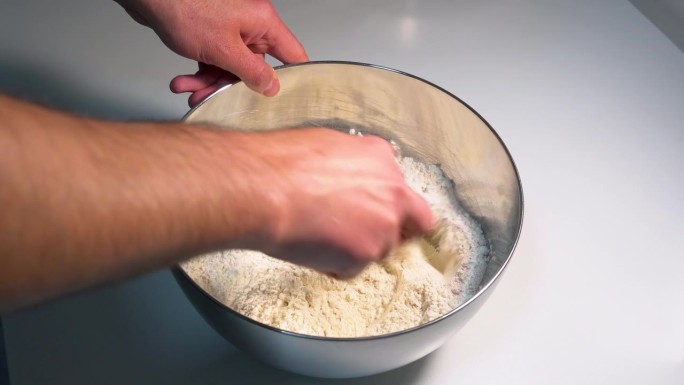 在白色表面的金属搅拌碗中混合配料，制作披萨和面包的面团