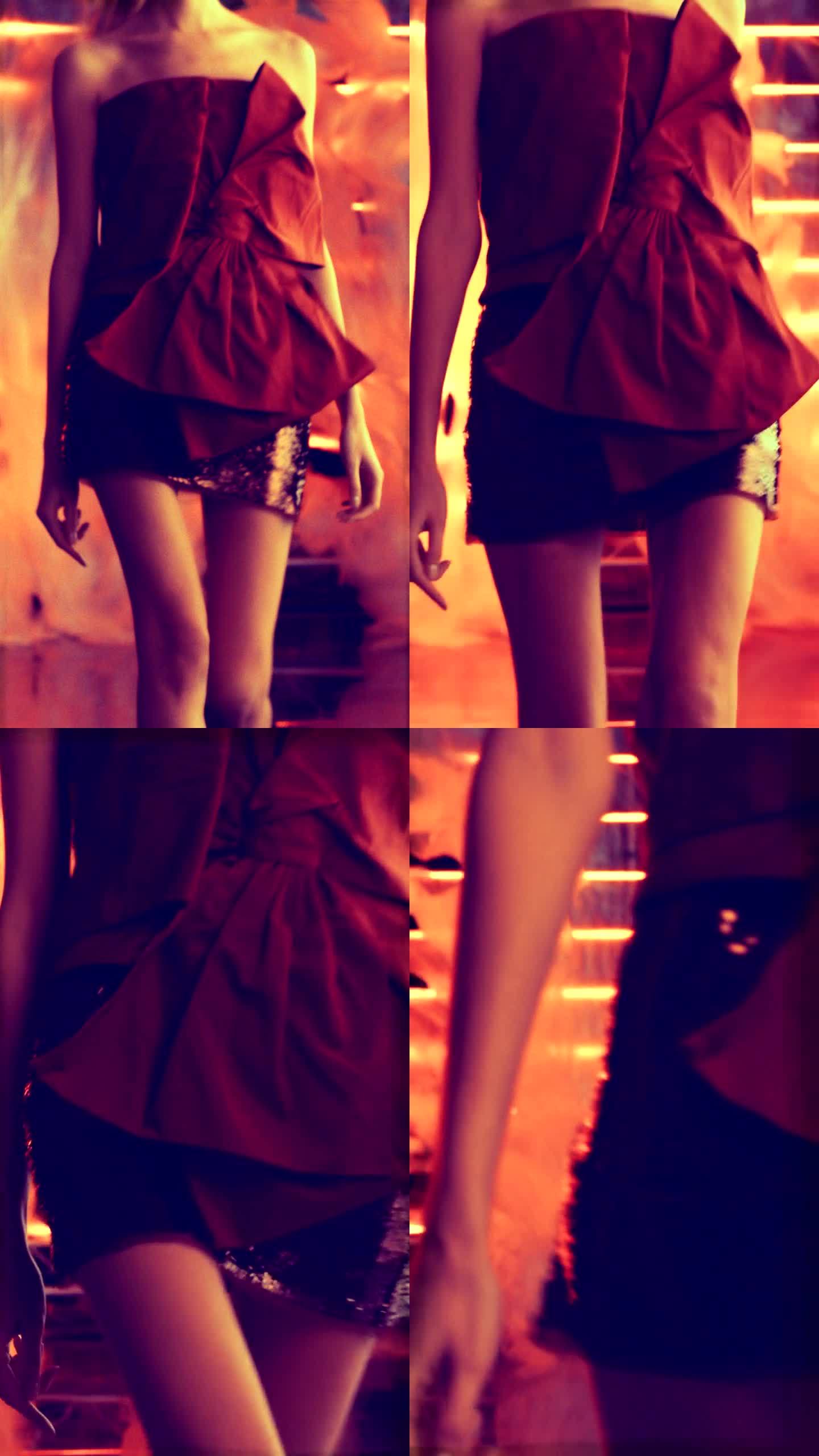 时装秀模特穿着高跟鞋和优雅的红色晚礼服走向镜头。背景中的抽象织物