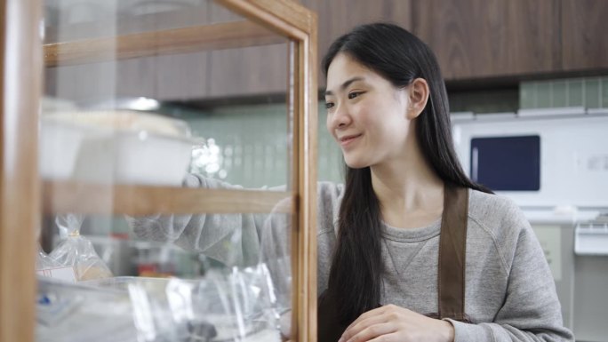 美丽的年轻亚洲女工作者站在超市烘焙部的货架上摆放新鲜的糕点或面包，面包店的小贩在咖啡馆的货架上摆放新