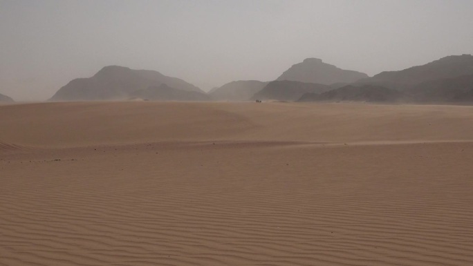 沙漠的沙尘暴。沙漠里沙丘里的沙在风中飘动。瓦迪拉姆沙漠。月亮谷。大型岩层的全景图。极端天气。