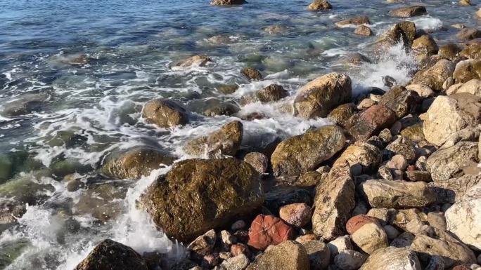 在阳光明媚的日子里，海浪卷到圆形的海石上。