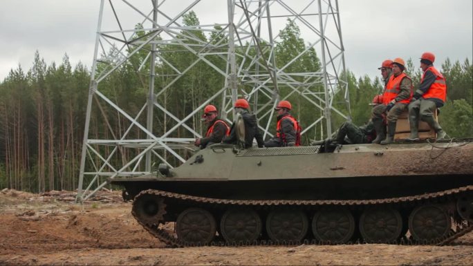 一队电工骑着一辆非军事化坦克沿着沼泽地的道路进行恢复电力的工作。