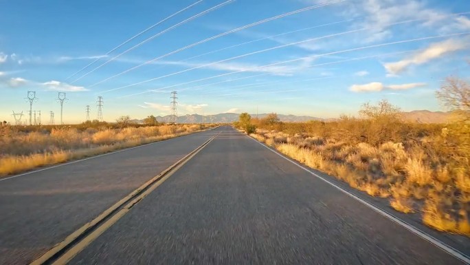 POV -在亚利桑那州南部索诺兰沙漠的柏油路和输电线路下行驶;傍晚时分，长长的影子映入眼帘，照亮了当