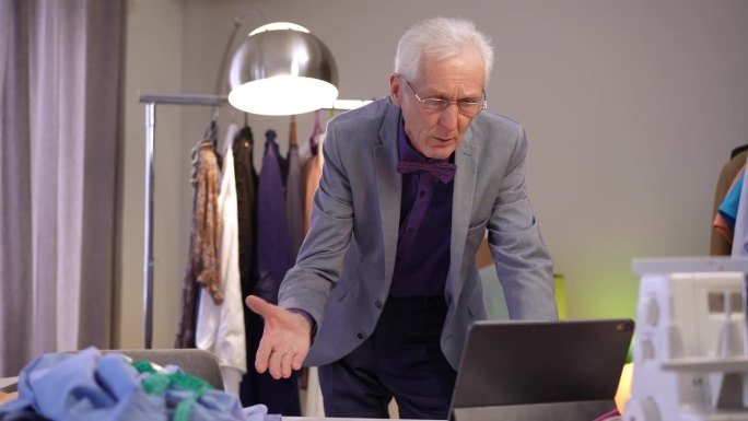 一位上了年纪的时尚男士靠在桌子前的平板电脑上，通过视频会议进行情感交流。