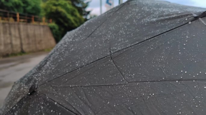 伞上的雨滴。黑色的伞，飞溅的雨滴，阴雨绵绵的天气。夏天，欧洲阴天下起了雨。背景是一条河和一座欧洲城市