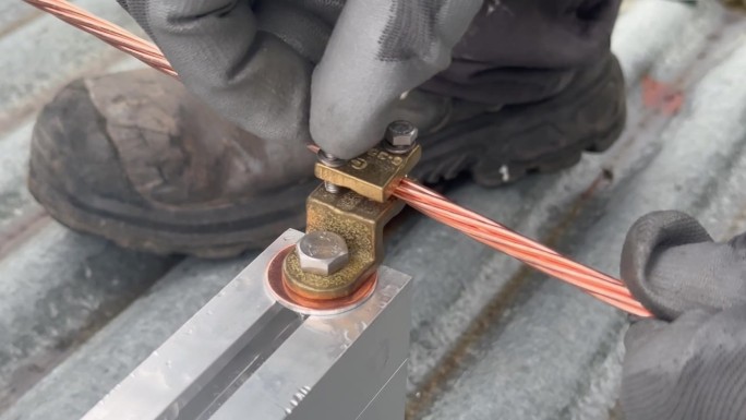 一名工人用手将接地编织线连接到支撑光伏板的铝轨上的特写。