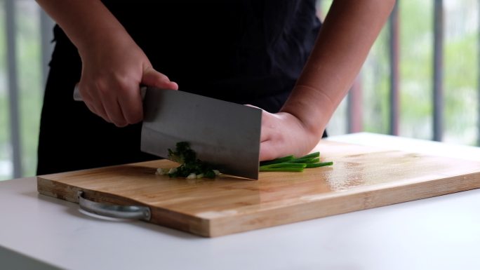 手拿菜刀在砧板上切小葱的特写