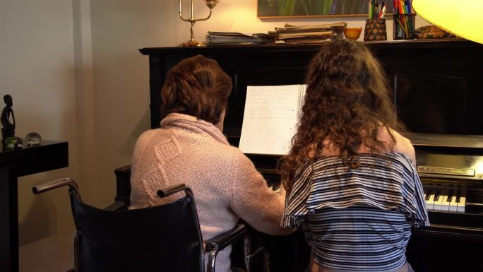 坐轮椅的老年妇女在家教年轻女子弹钢琴