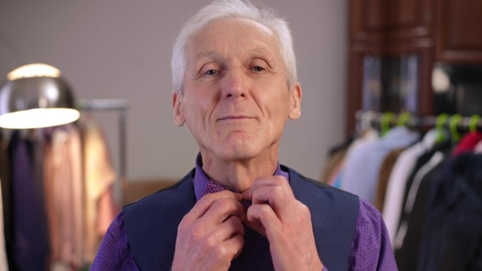 特写镜头。一位穿着时髦的老人正整理着他的紫色领结。男人微笑着看着镜头。