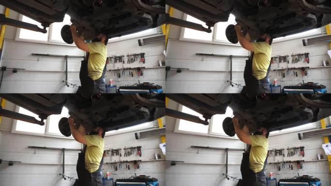 汽车维修厂的机械师用扳手修理汽车。穿着制服的专业修理工在车库的起重车辆下面工作。有人在拧紧螺栓。汽车