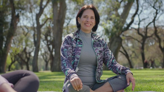 微笑的成熟女人在公园瑜伽课上摆姿势拍照