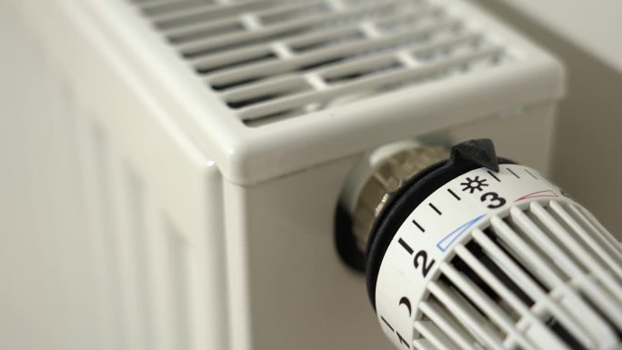 一个人通过将恒温散热器阀门控制设置到最小设置来关闭暖气。能源危机时关掉公寓的暖气。节能