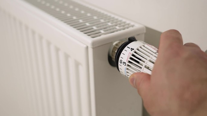 一个人通过将恒温散热器阀门控制设置到最小设置来关闭暖气。能源危机时关掉公寓的暖气。节能