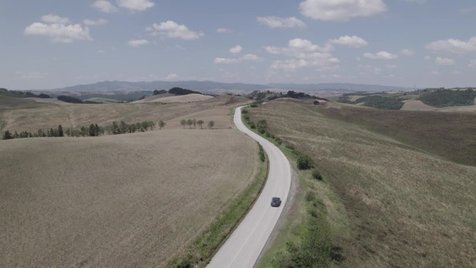 无人机拍摄的蜿蜒的道路和金色的农场在意大利托斯卡纳风景晴朗的一天，蓝天和云在地平线上LOG