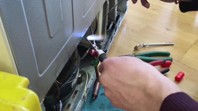 通过给氟利昂管充电来修复冰箱冷却不足的问题。师傅用烙铁把一根管子接上氟利昂。
