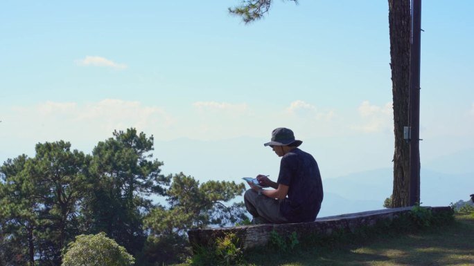 数字游牧民和旅行的概念与单独的自由职业者男人坐在木头和使用平板电脑工作从户外层山的背景