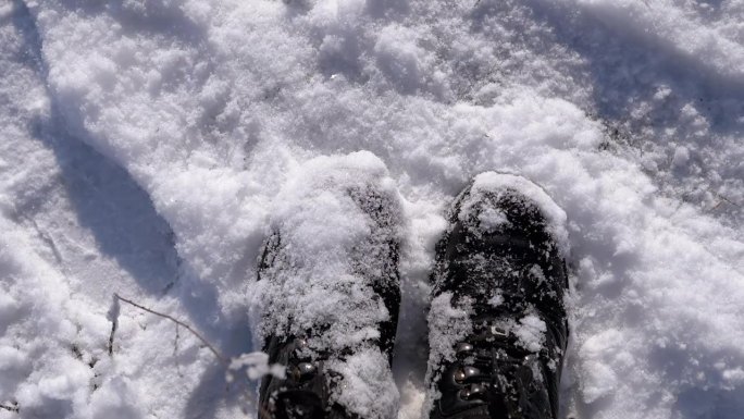 俯视图女子在雪中站在雪堆上，抖掉黑色靴子上的雪